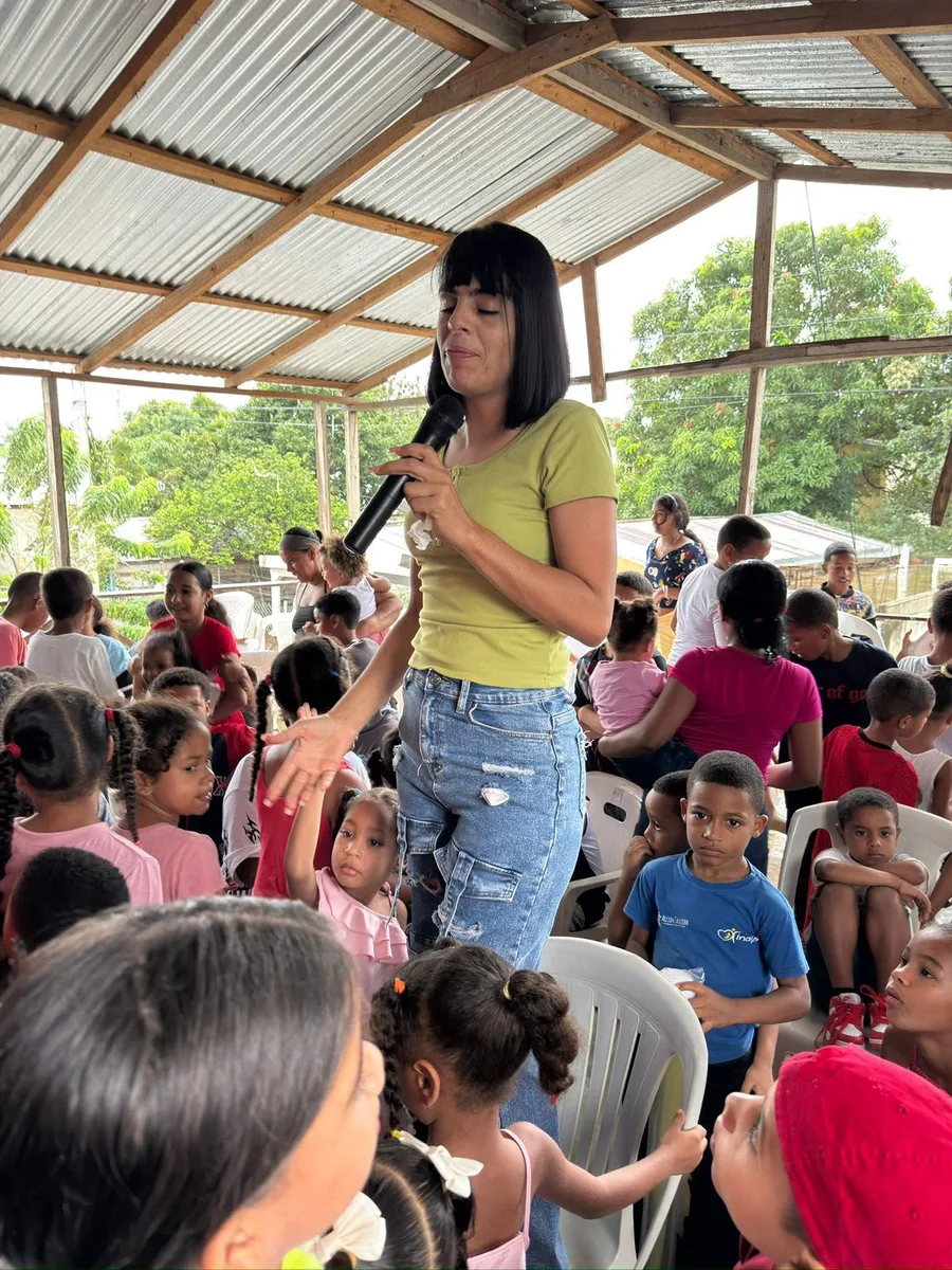 Voluntaria hablando con micrófono ante decenas de niños en evento comunitario
